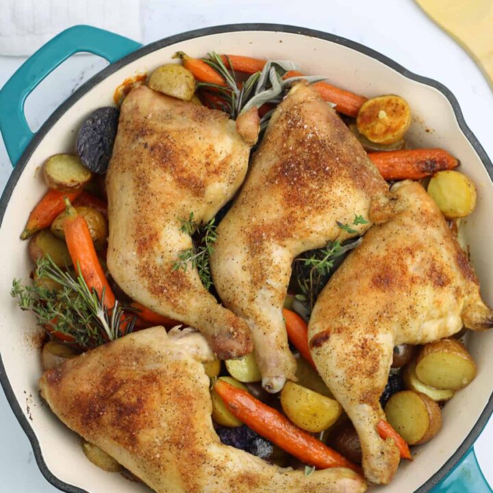 skillet of cooked chicken quarters with potatoes and carrots