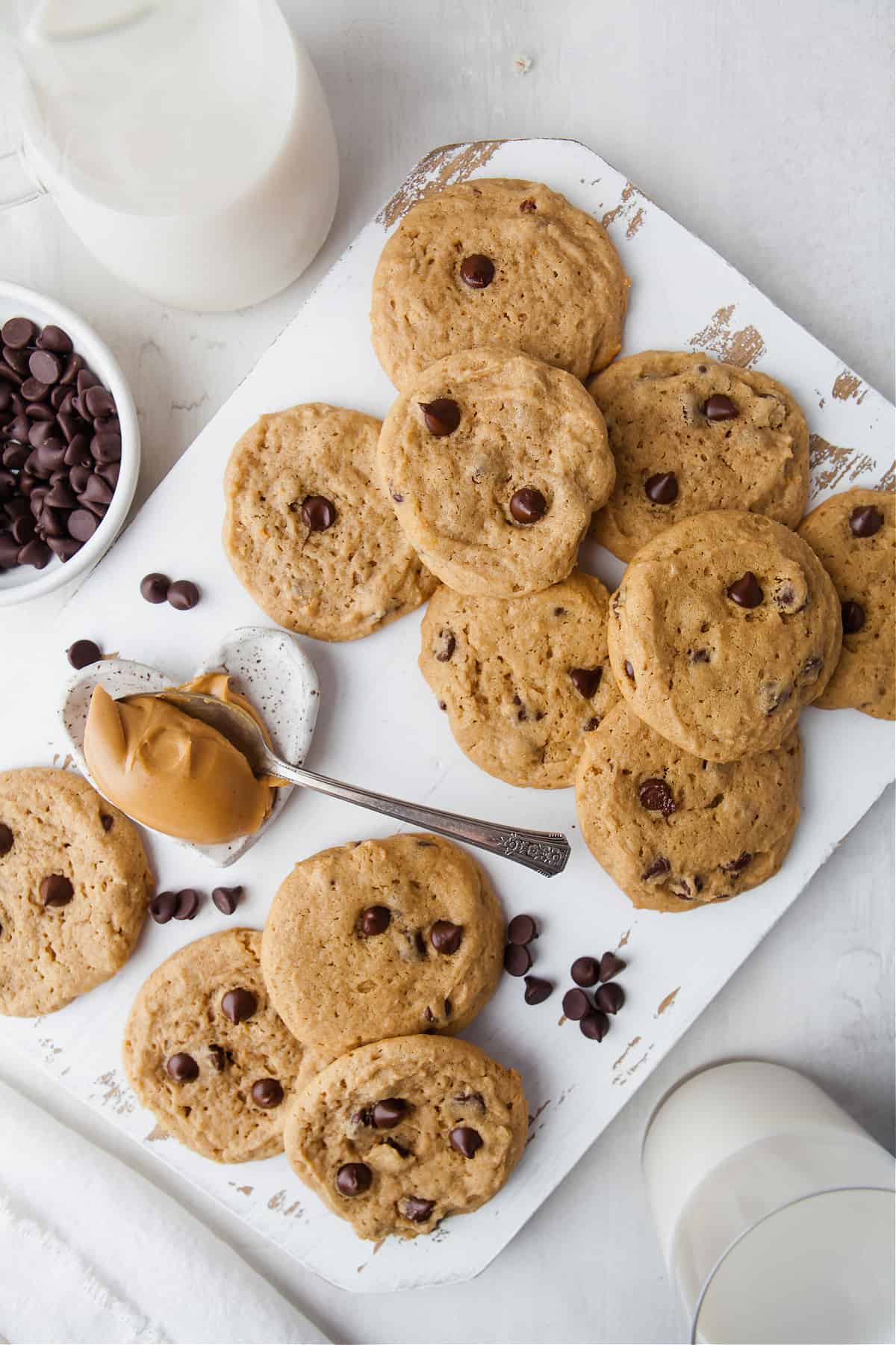 a top view of cookies on a white board next to a bowl of chocolate chips and a glass ofmilk