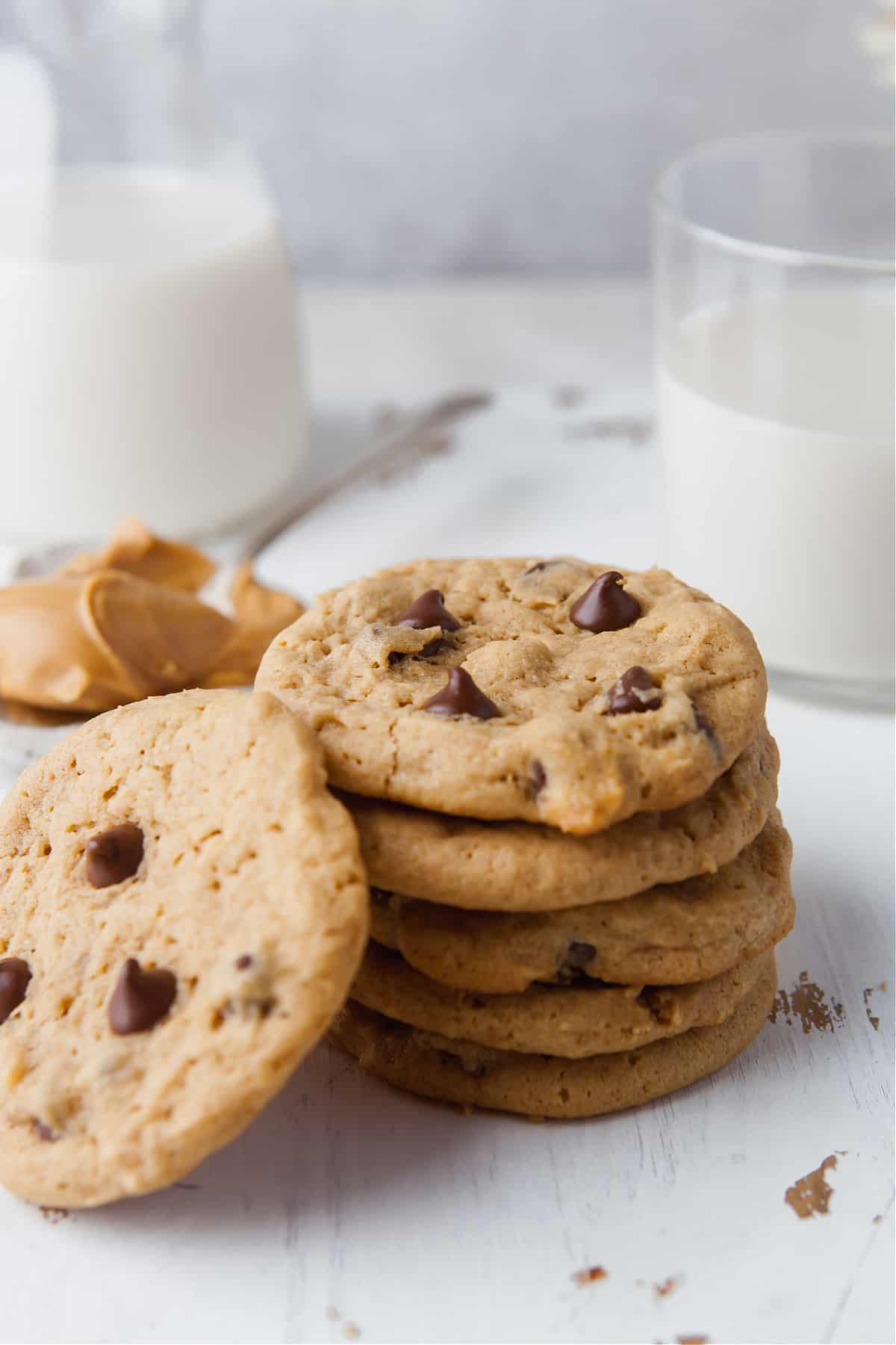 a stack of cookies on a white table next to a glass of milk