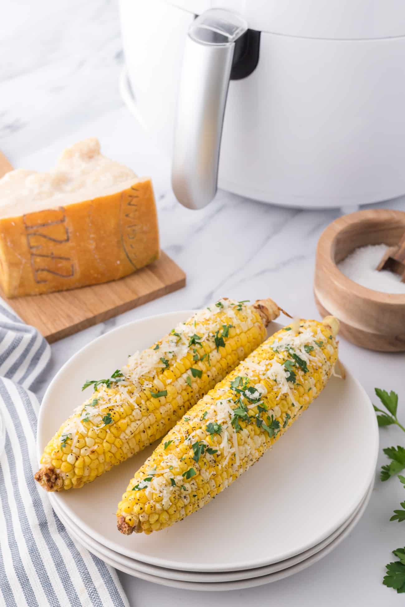 two corn on the cob on a stack of white plates next to an air fryer