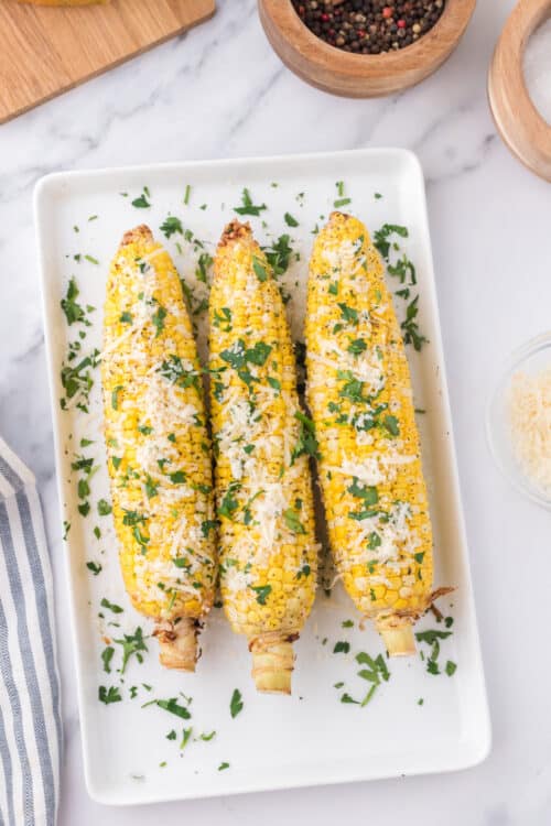three ears of corn on a white serving tray