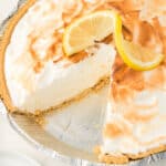 a lemon pie with a slice taken out of it with a fresh lemon wedge on top of the pie.
