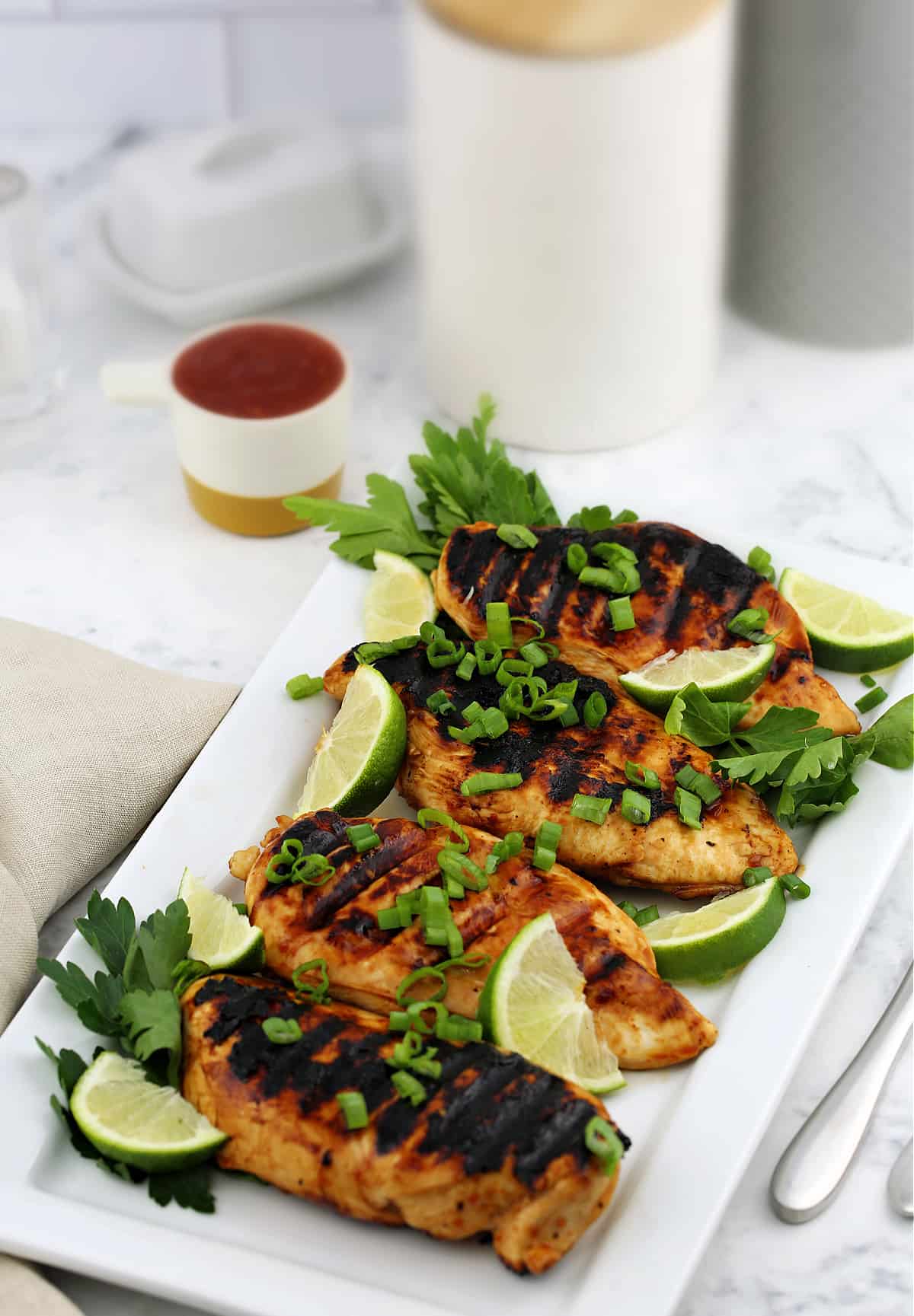 whole grilled chicken breasts on a white tray with lime slices
