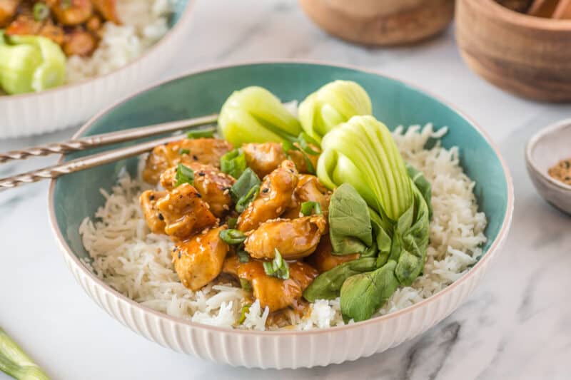 A bowl of food on a plate, with General Tso\'s chicken