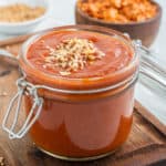 a jar of homemade sauce on a wooden cutting board.