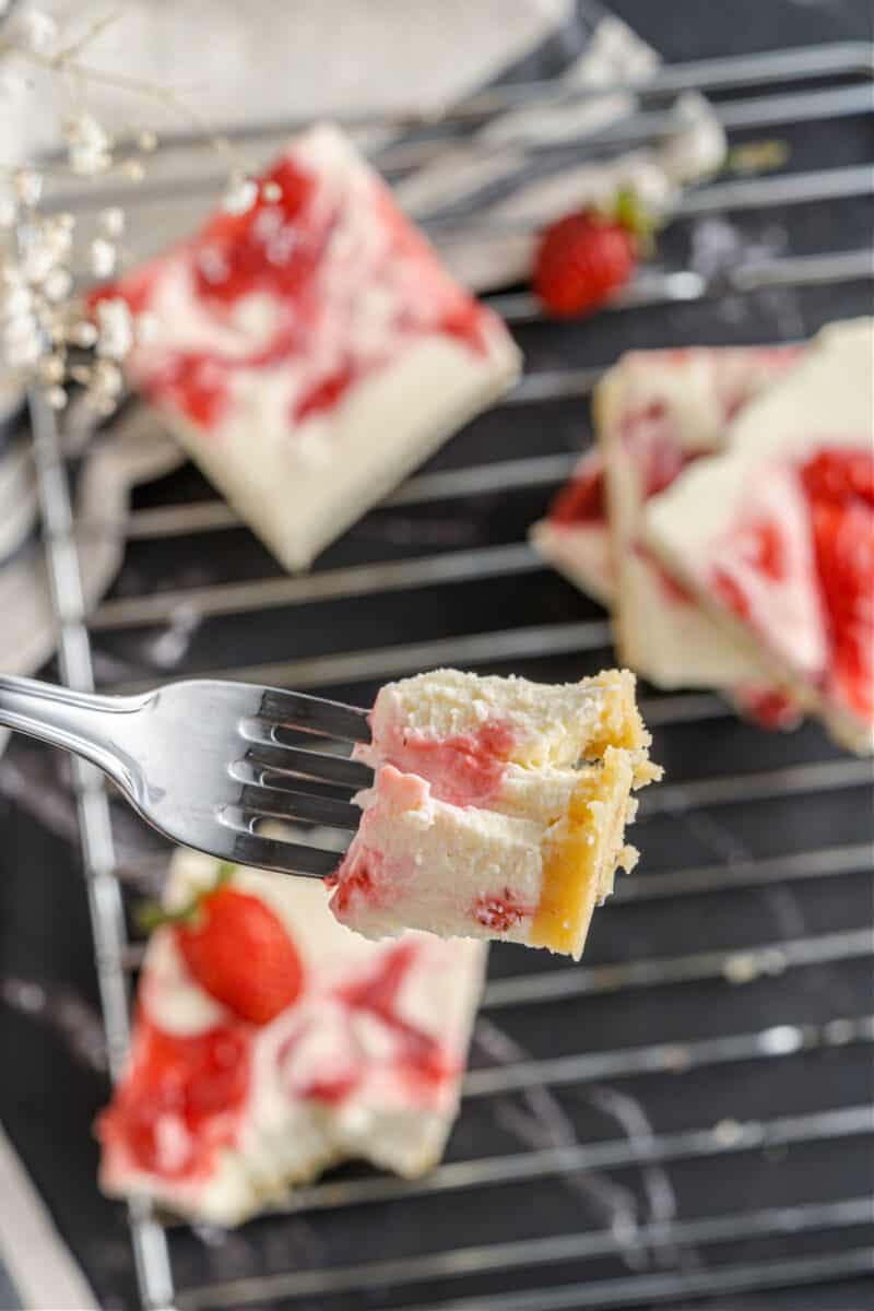 A piece of cheesecake on a plate with a fork, with Strawberry and Cream