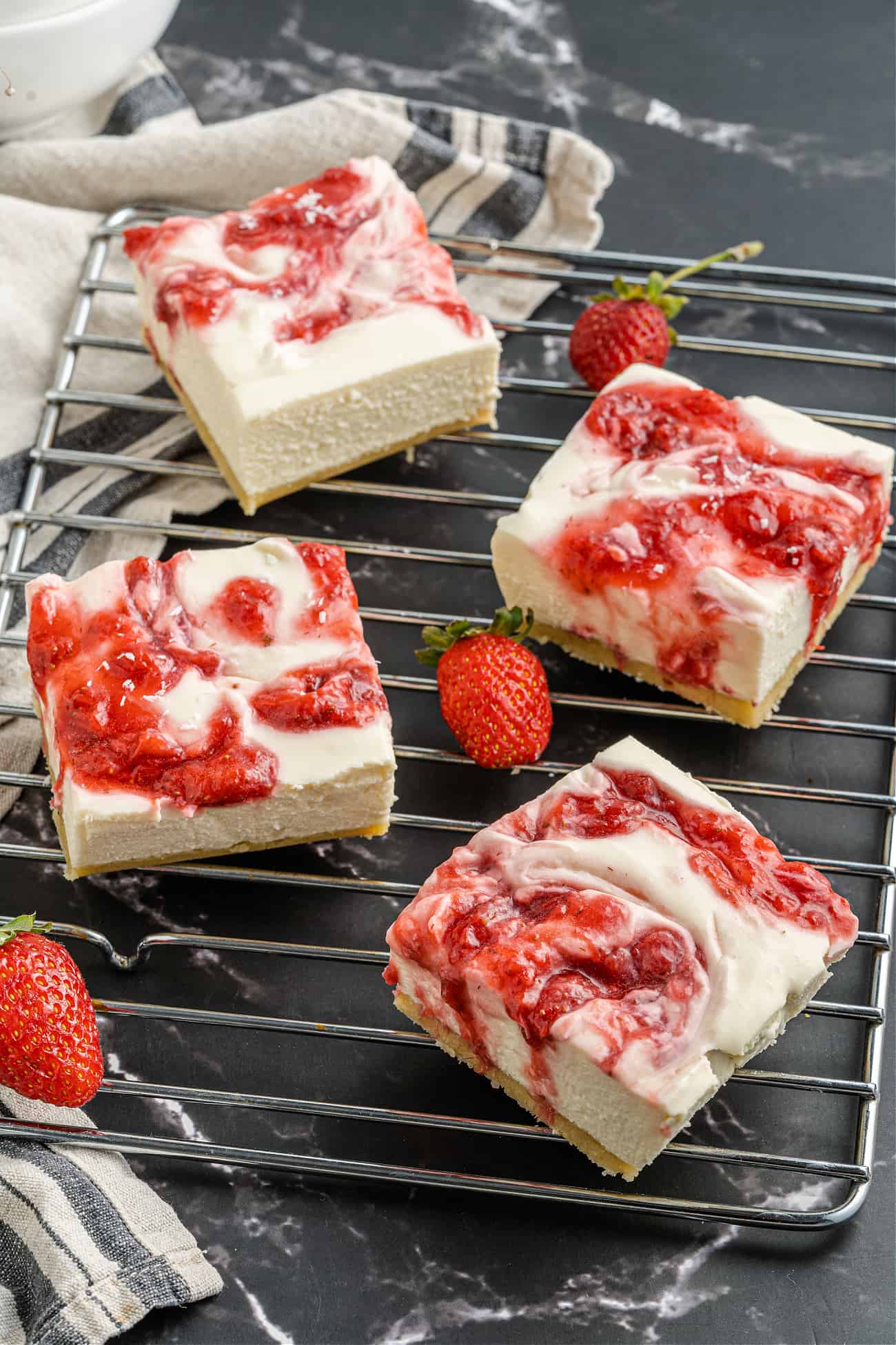 Cut strawberry cheesecake bars on a cooling rack with fresh strawberries.
