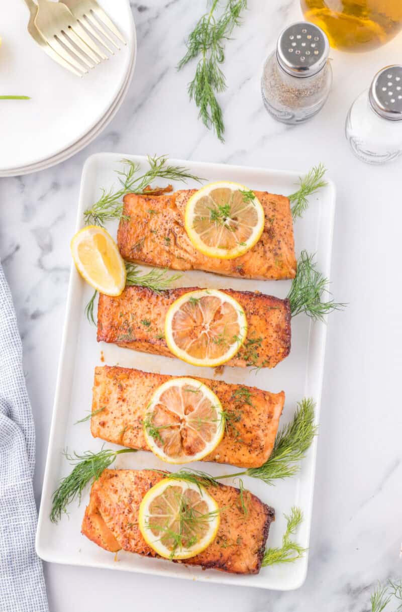 a rectangle white plate with 4 pieces of salmon with sliced lemon
