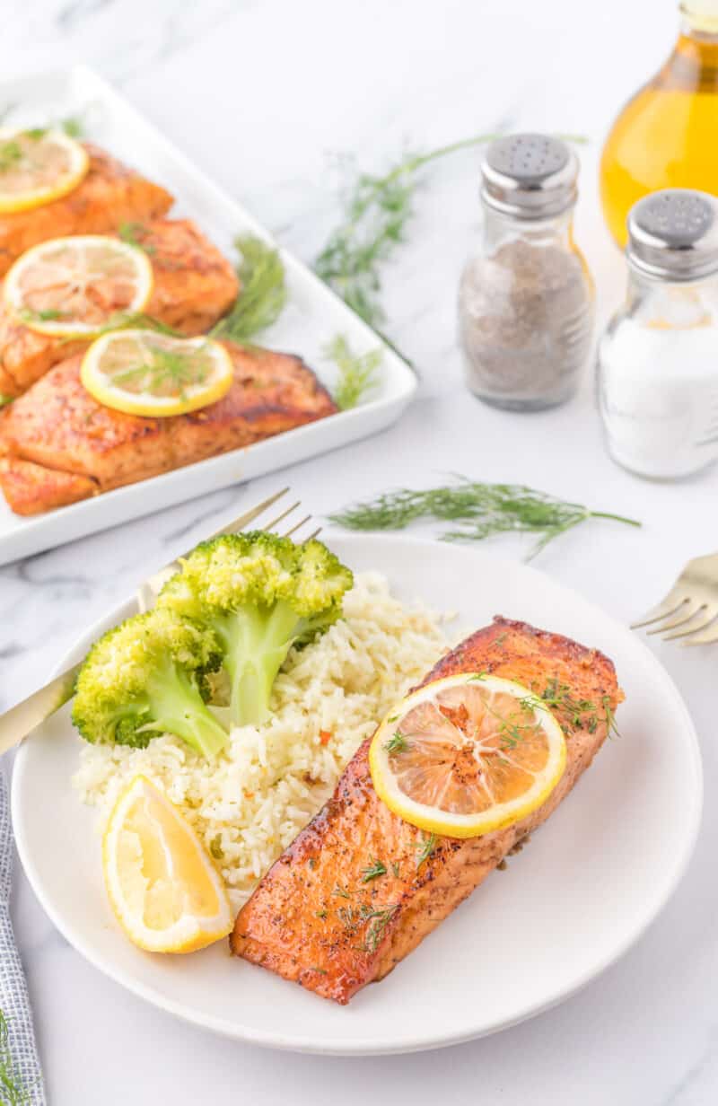 a piece of salmon with lemon on a plate with rice and broccoli