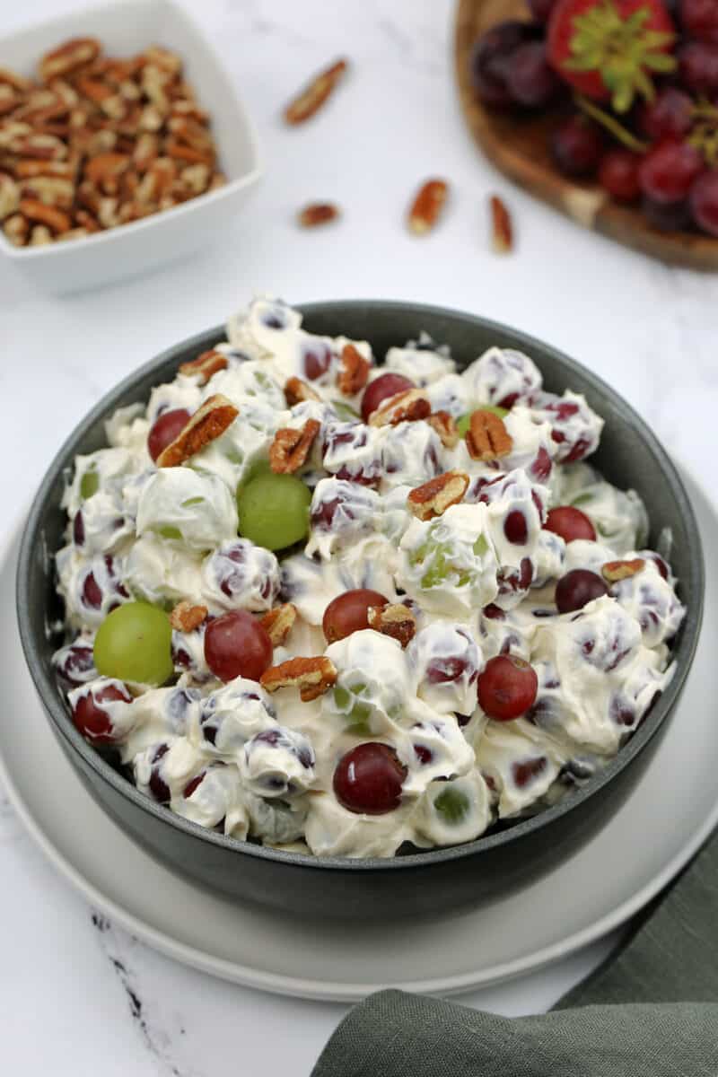 food in a bowl on a table, with grape salad and pecans