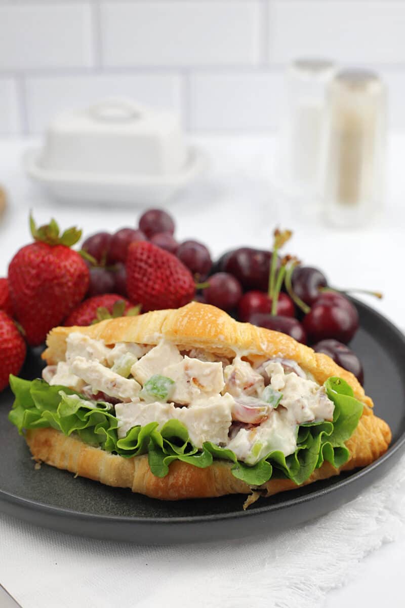 chicken salad croissant sandwich with fresh fruit on the plate