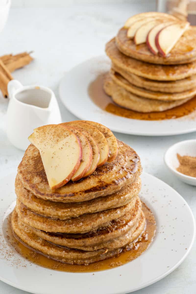 stacks of pancakes on plates on a table, with Oat Flour Pancakes and maple syrup