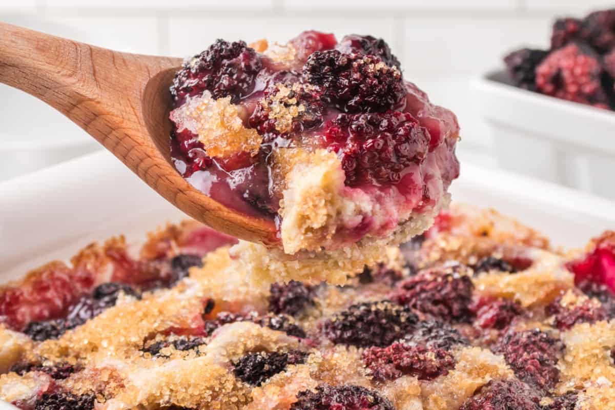 blackberry cobbler in a white dish with a wooden spoon.