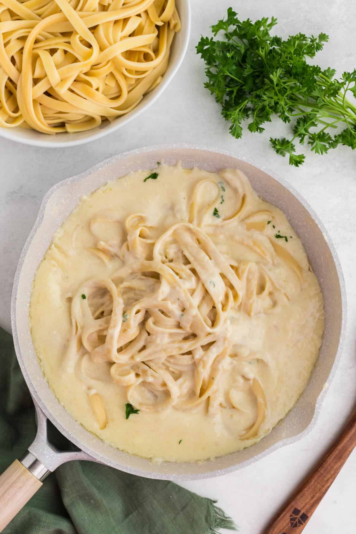 a pan of cooked noodles in a white sauce beside a bunch of fresh parsley.