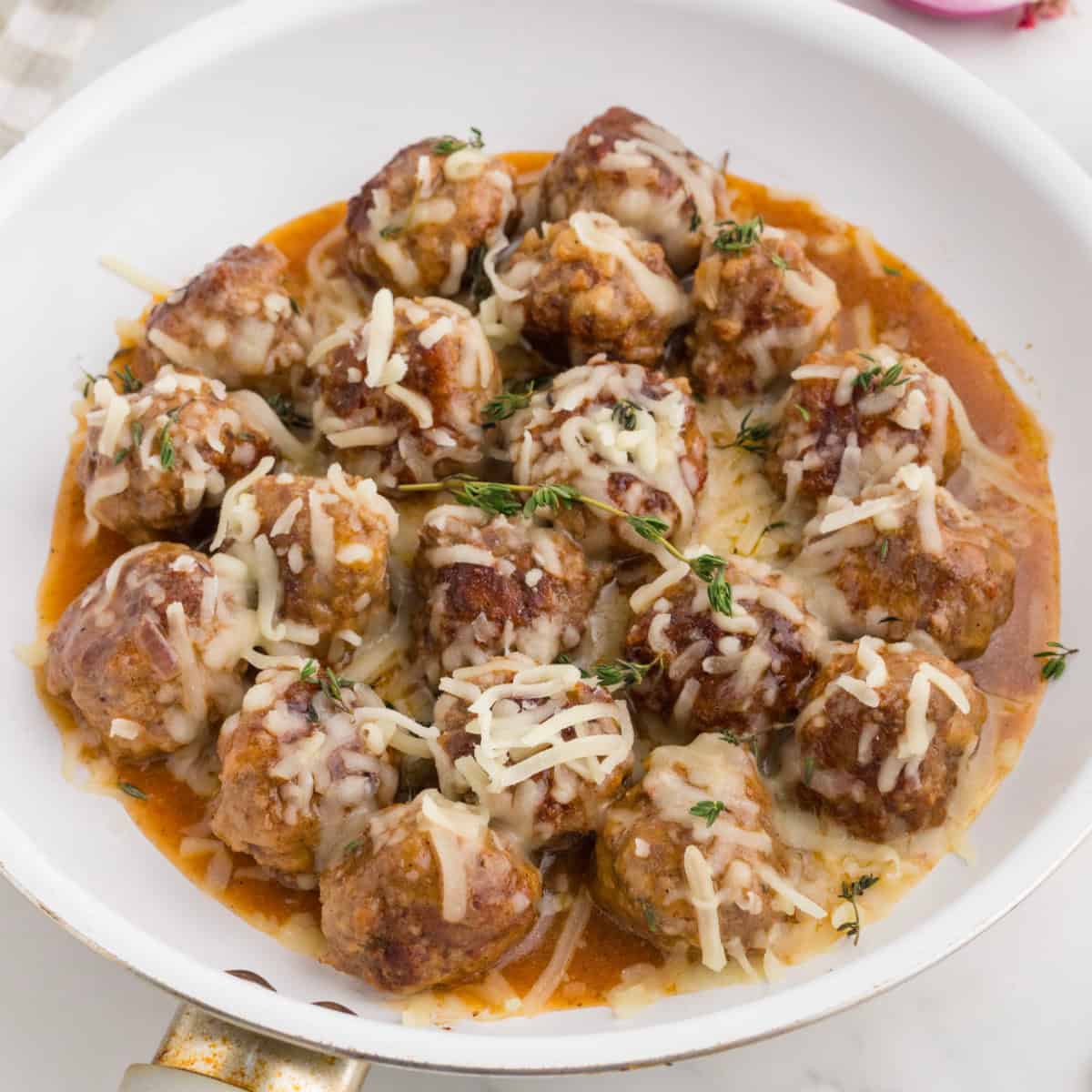 freshly cooked meatballs in a white skillet covered with melted cheese.