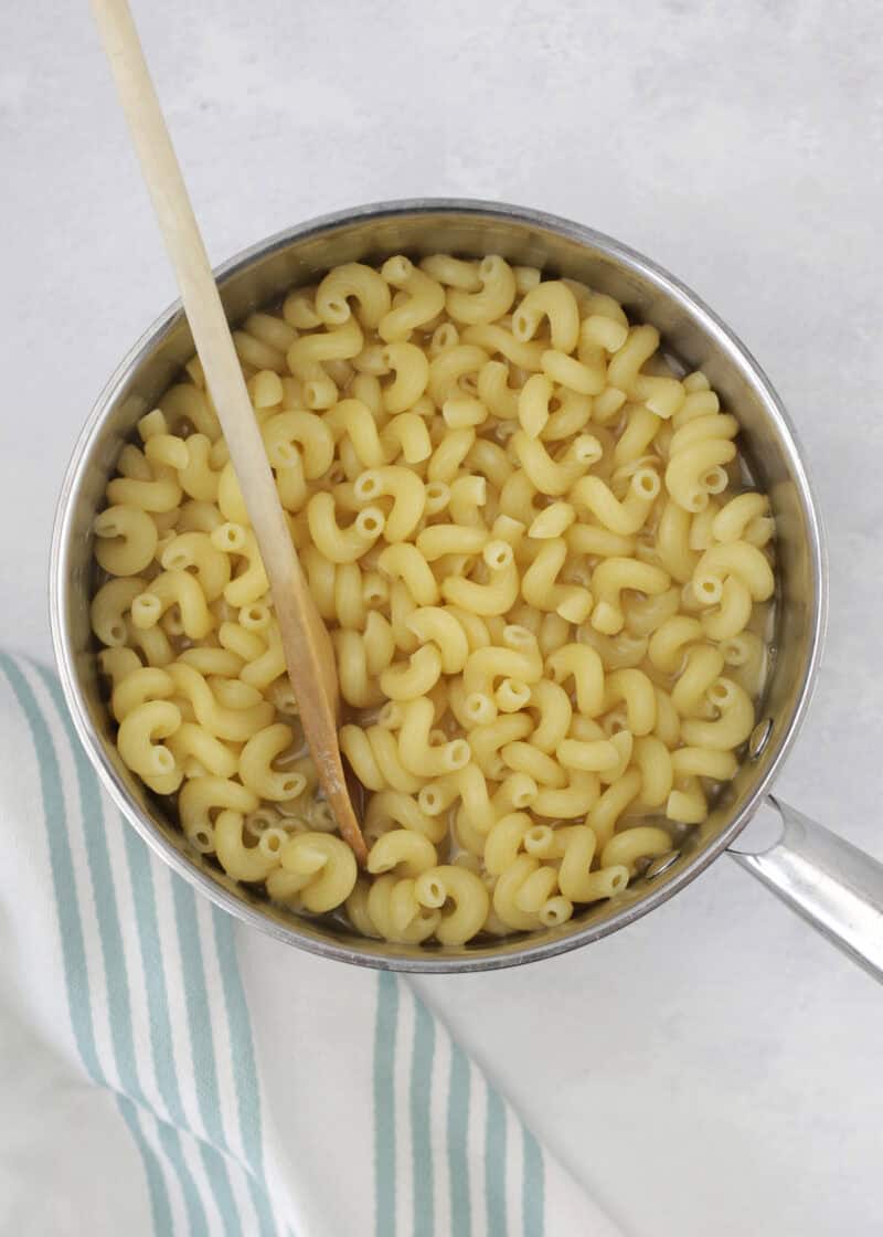 cooked spiral noodles in a large stainless silver pot with a wooden spoon