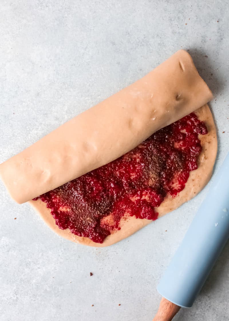 raspberry filling on top of dough that is being rolled.