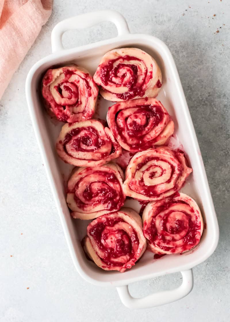 raspberry cinnamon rolls in a white rectangular baking dish on a table.