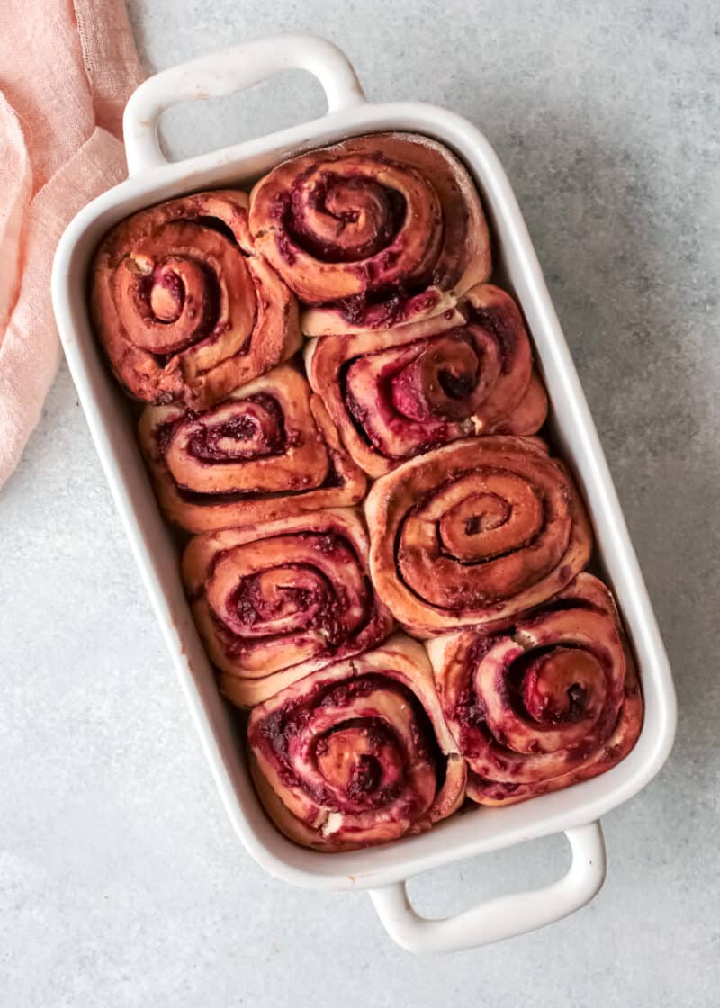 raspberry cinnamon rolls in a white rectangular baking dish on a table.