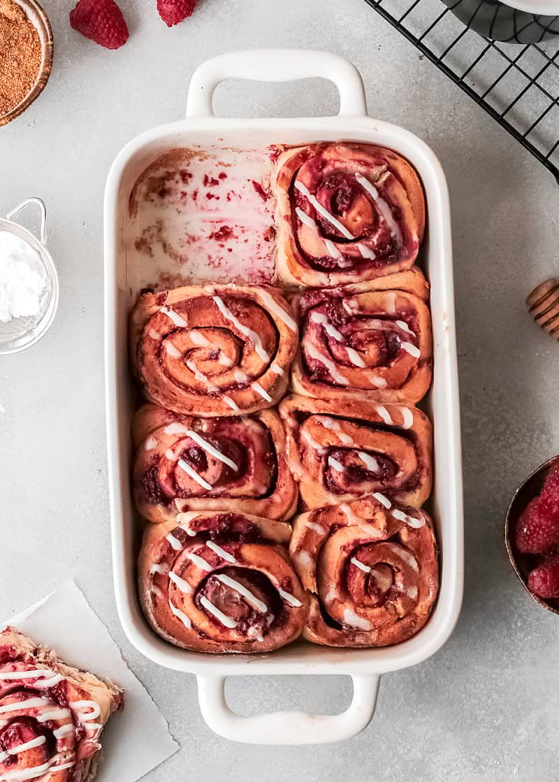 raspberry cinnamon rolls with a cream cheese glaze in a white rectangular baking dish on a table.