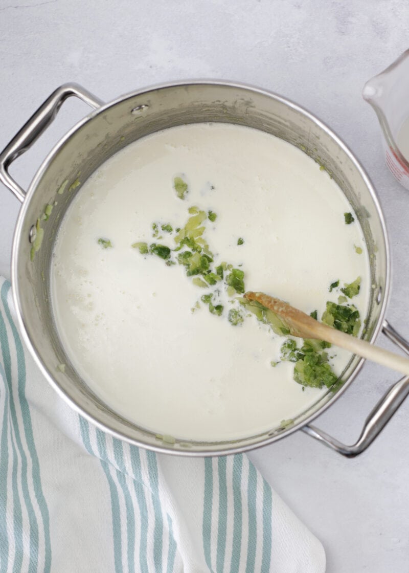 mac and cheese sauce with jalapeno and onion in a large sauce pot with a wooden spoon on a table