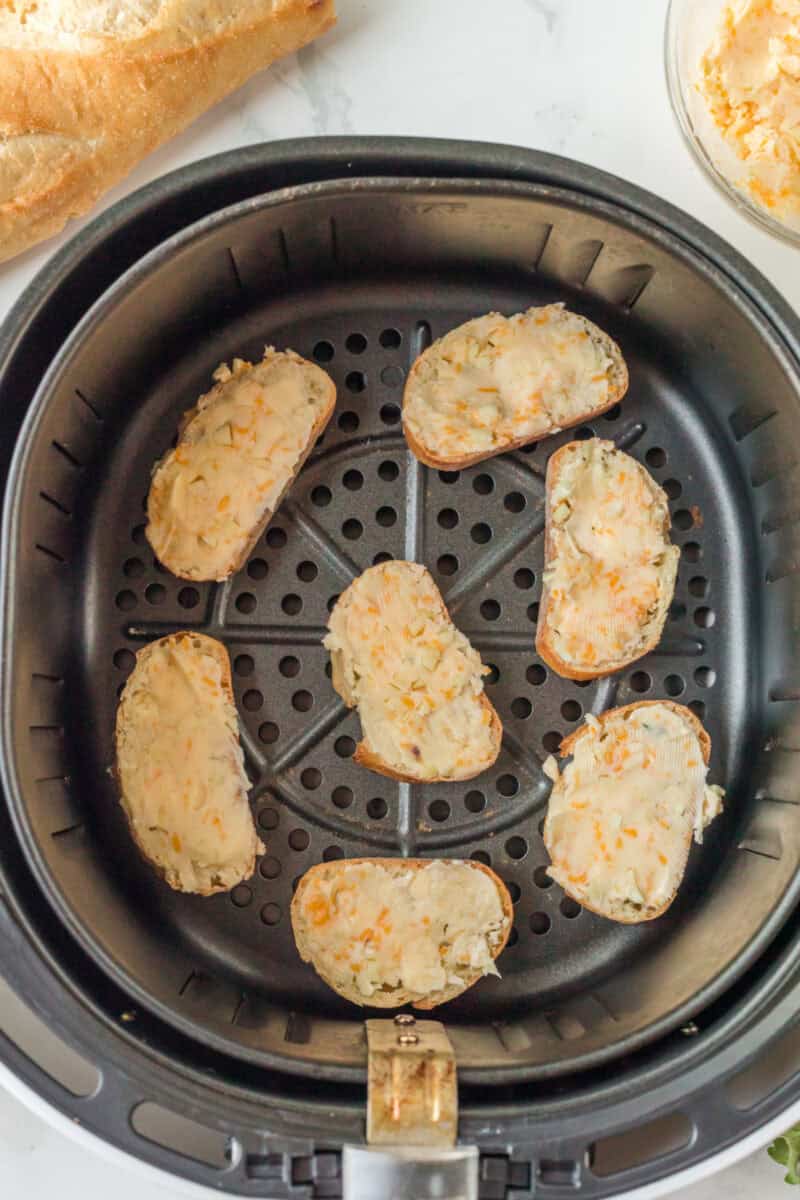 uncooked slices of bread with a cheese garlic butter on top, in a black air fryer basket.