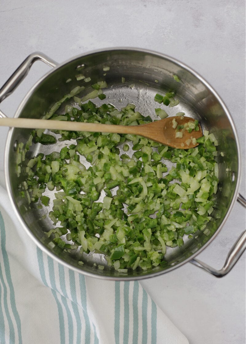 cooked chopped jalapeno and onion in a large silver sauce pot with a wooden spoon