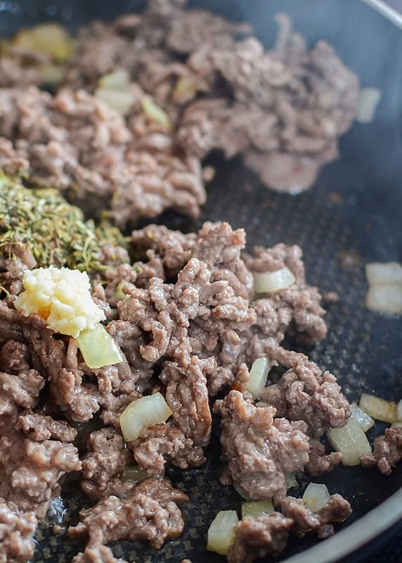 cooked ground beef in a frying pan with minced garlic and cooked onions.