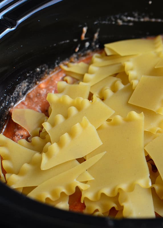 pieces of uncooked lasagna noodles on top of sauce in a black crockpot.