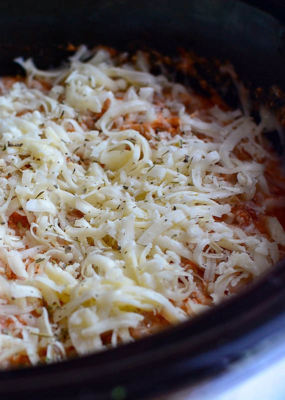 uncooked shredded cheese on top of a sauce in a black crockpot.