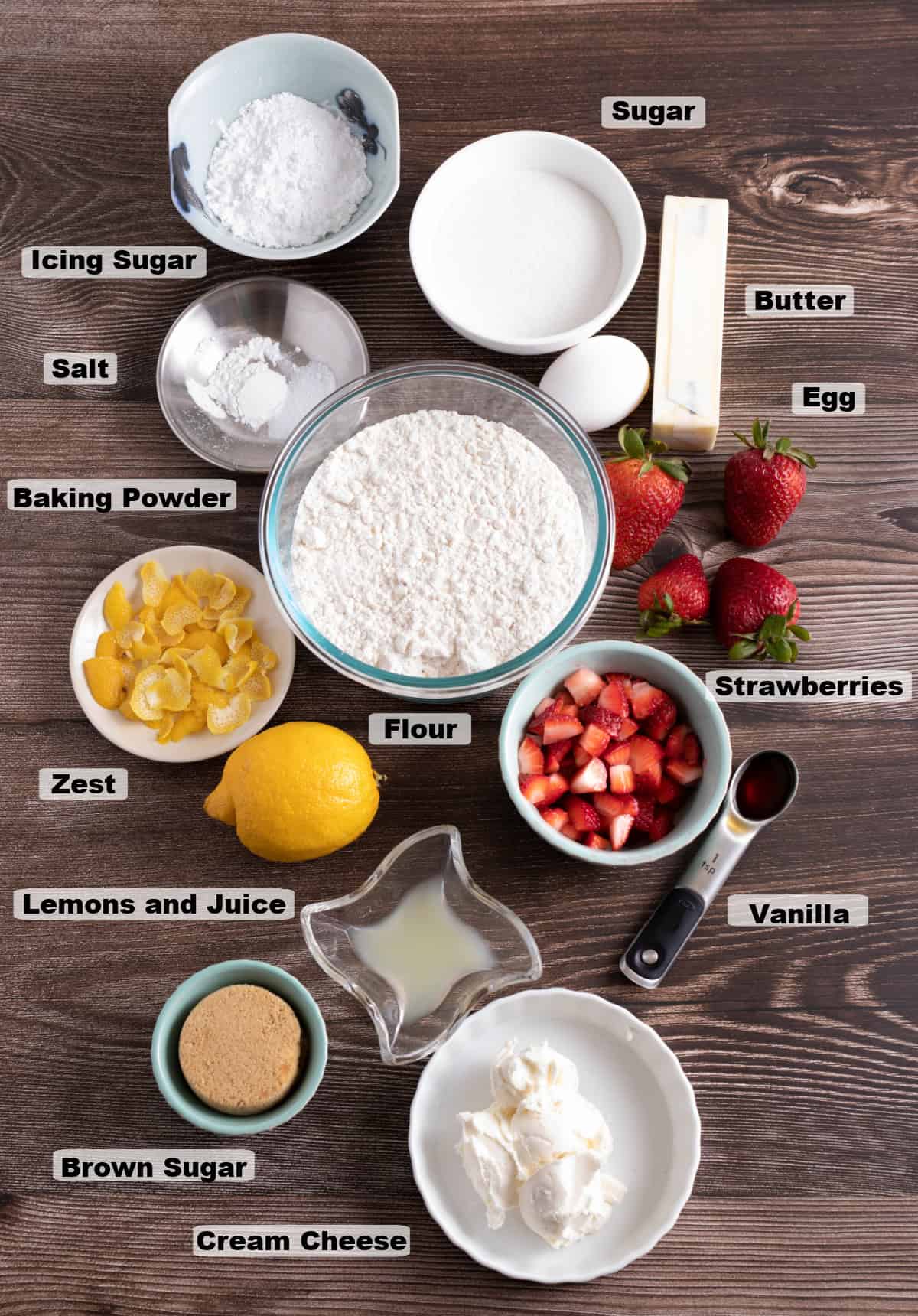 ingredients on a table to make Strawberry Lemonade Cream Cheese Cookies such as a bowl of flour, fresh lemons, butter, eggs, cut strawberries.
