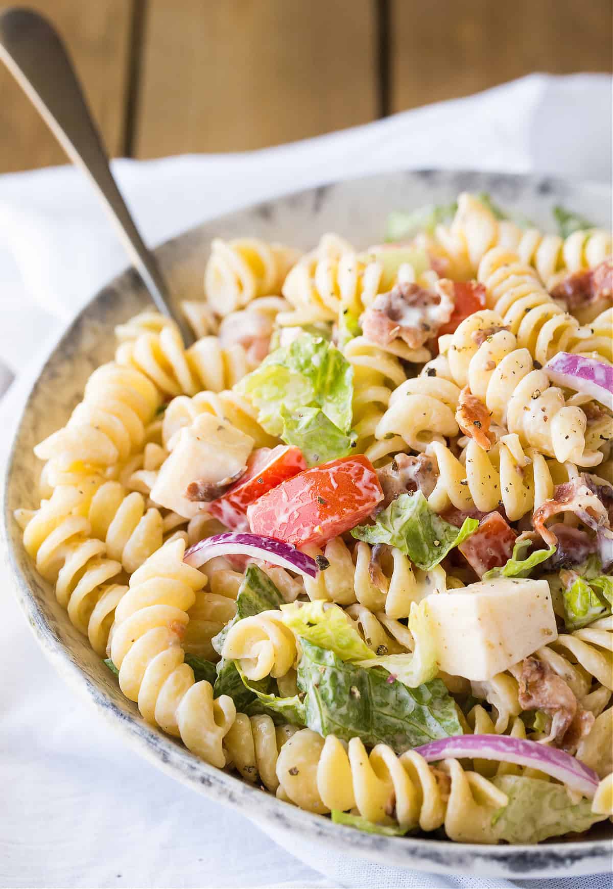 a bowl of pasta salad on a table with a spoon in it.