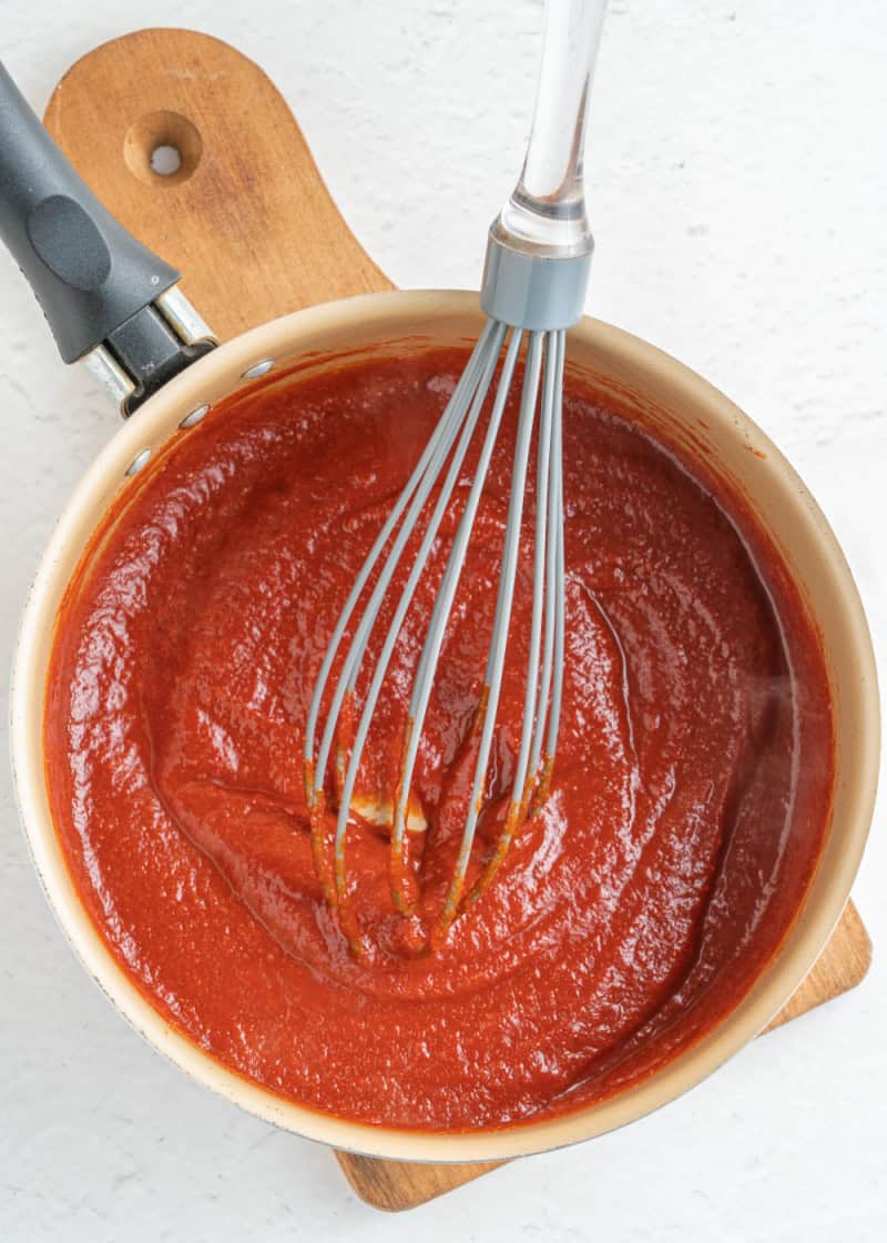 tomato type sauce in a saucepan with a metal whisk.