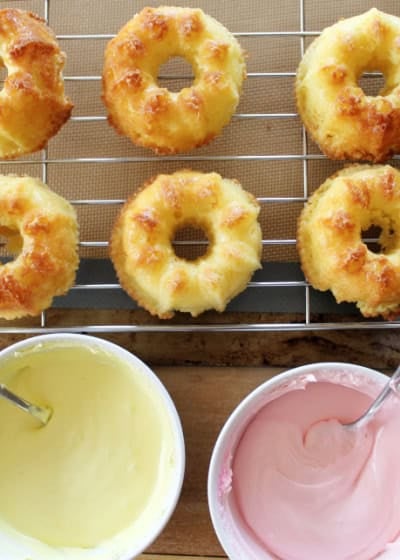 small bundt cakes on a cooling rack beside two bowls of icing, one yellow and pone pink.