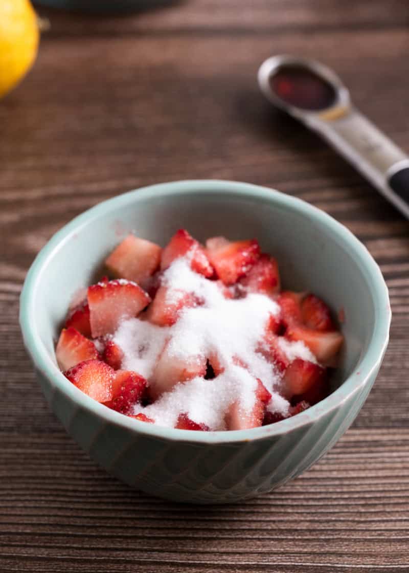 a small bowl with cut strawberries inside and sprinkled granulated sugar on top.