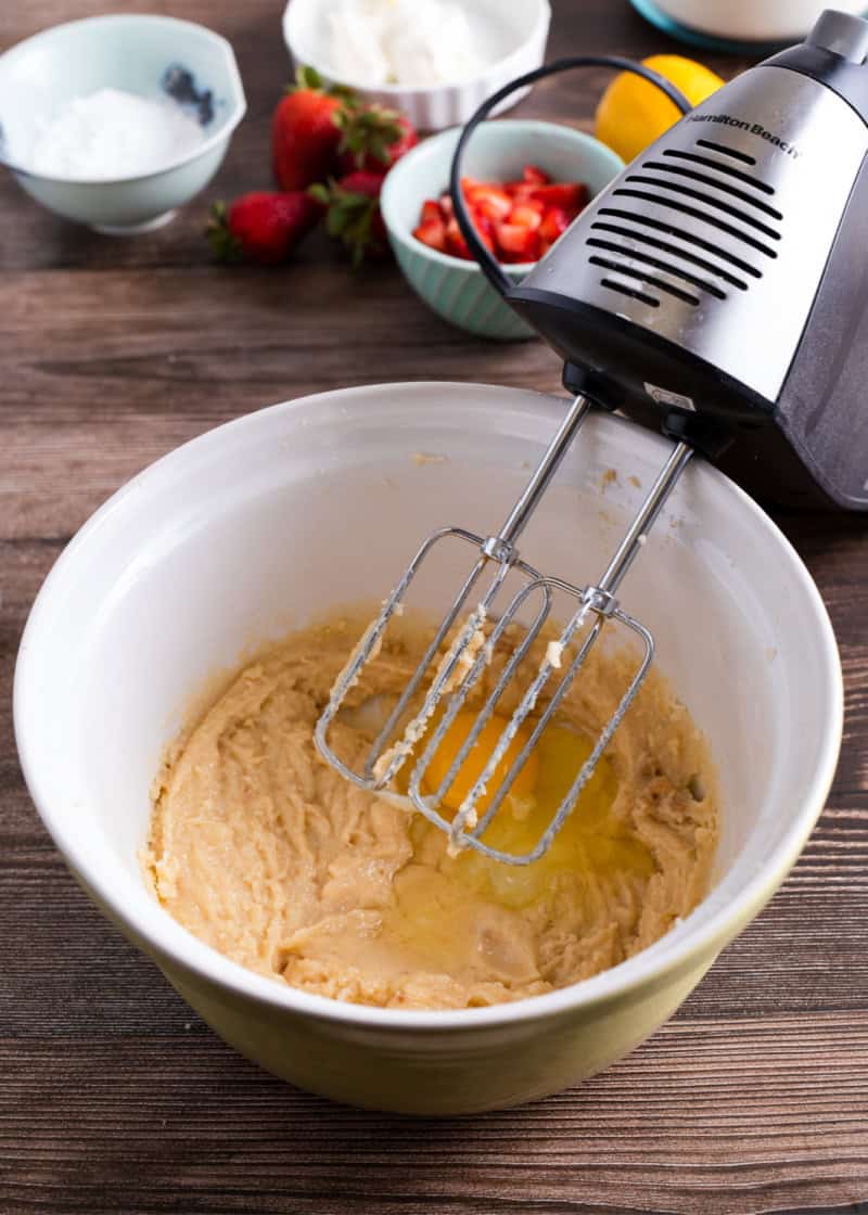 a mixture in a bowl with a raw egg in it being mixed with an electric mixer.