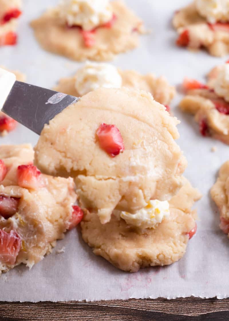 flattened uncooked cookie dough on a metal spatula being put onto parchment paper.
