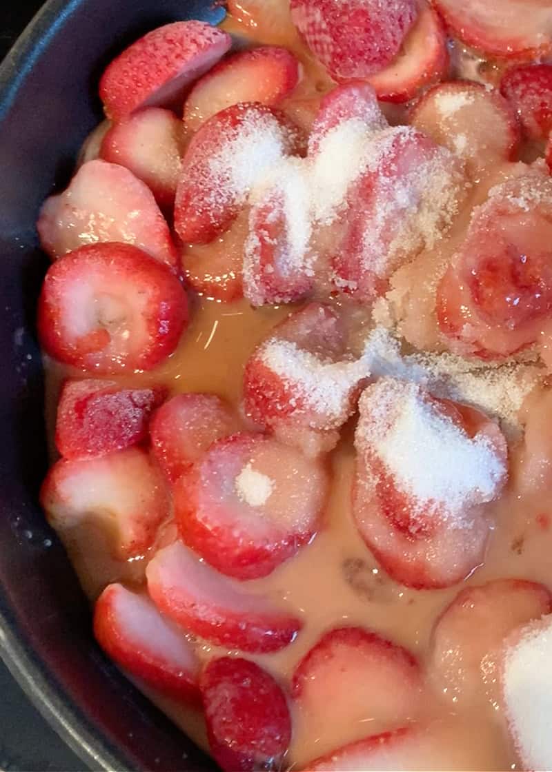 fresh strawberries and sugar being cooked in a frying pan.