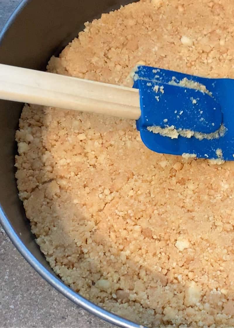 cookie base being spread into a springform pan with a rubber spatula.