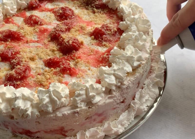Whipped cream decoration being added to a strawberry shortcake ice cream cake.