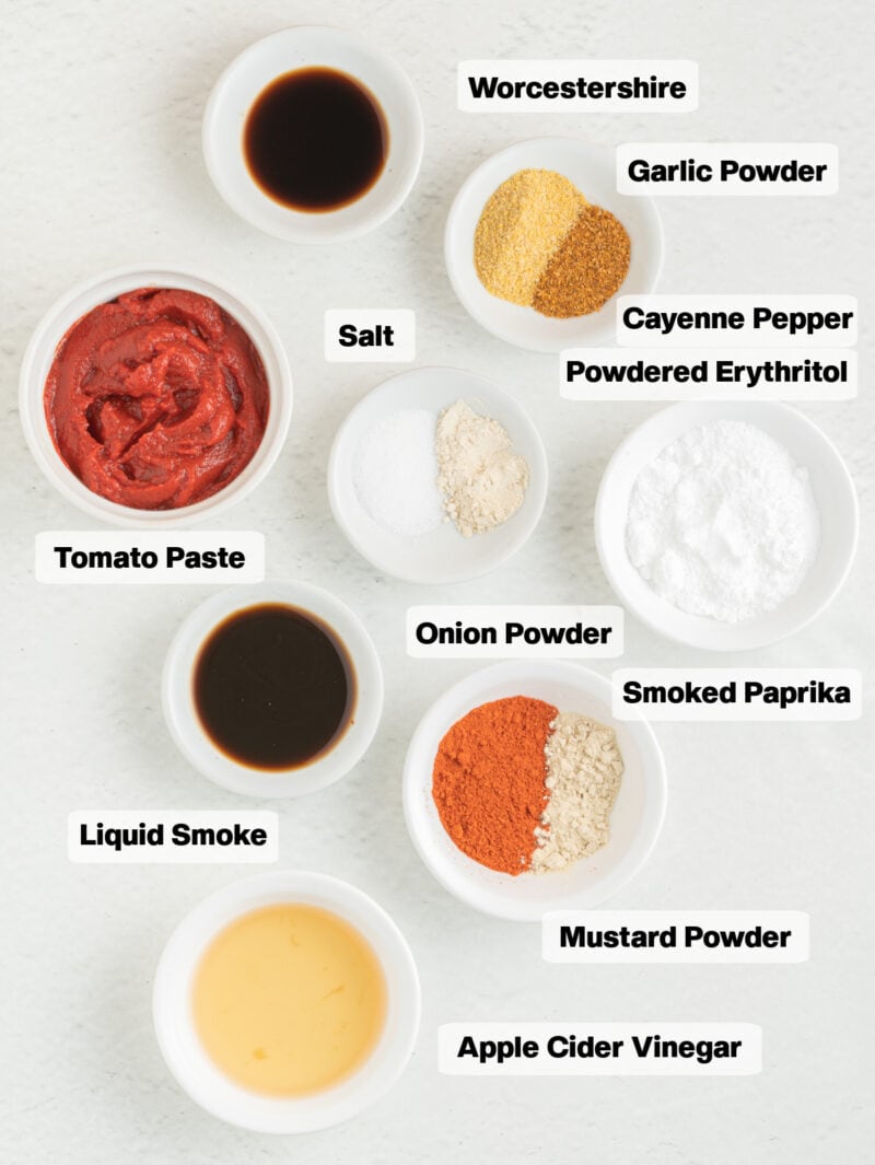 ingredients on a table to make keto bbq sauce including tomato paste, spices, powdered erythritol and liquid smoke.