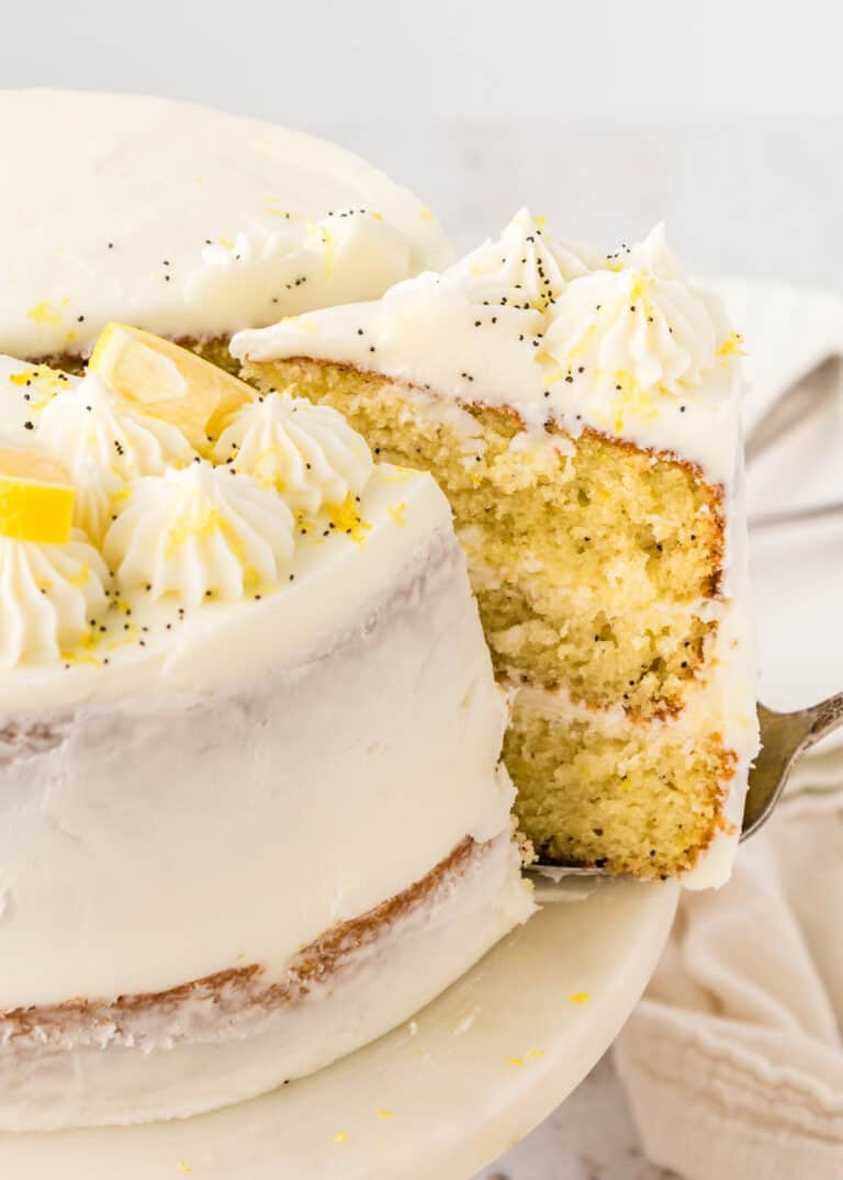 A slice of lemon poppy seed cake being cut from a whole cake.