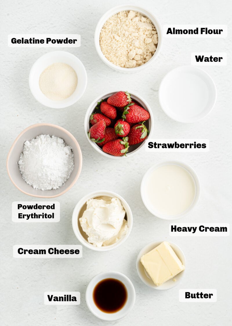 Ingredients on a table to make cheesecake bars such as flour, butter, strawberries, cream, and vanilla.