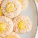 Lemon Thumbprint Cookies sprinkled with powdered sugar stacked on a white plate.