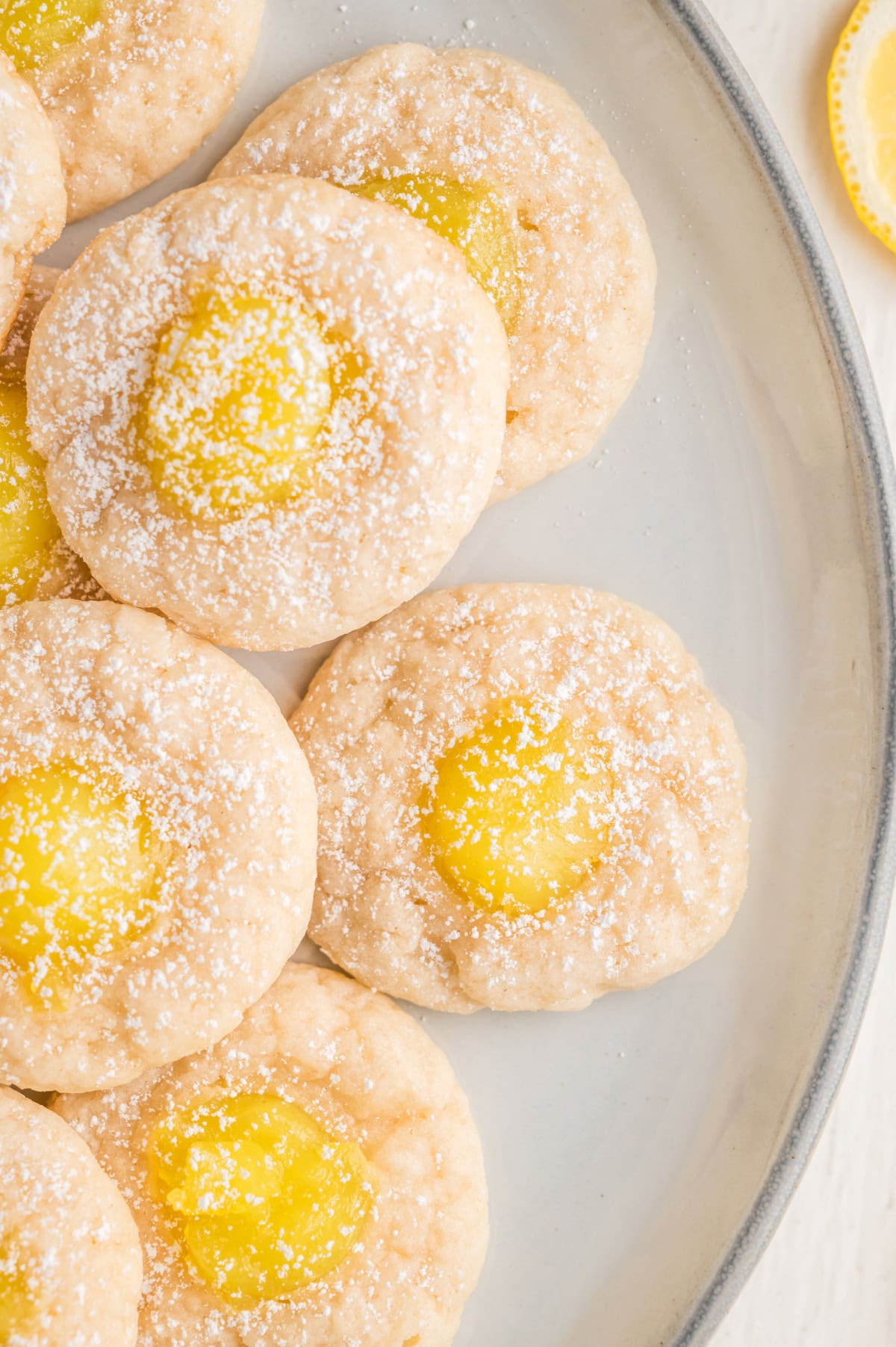 Lemon Thumbprint Cookies sprinkled with powdered sugar stacked on a white plate.