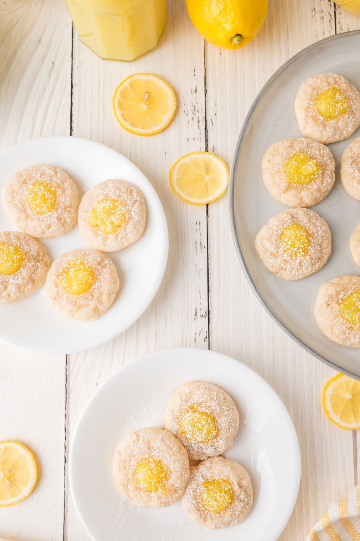 Lemon Thumbprint Cookies sprinkled with powdered sugar on white plate and a round baking pan surrounded by fresh lemon slices.