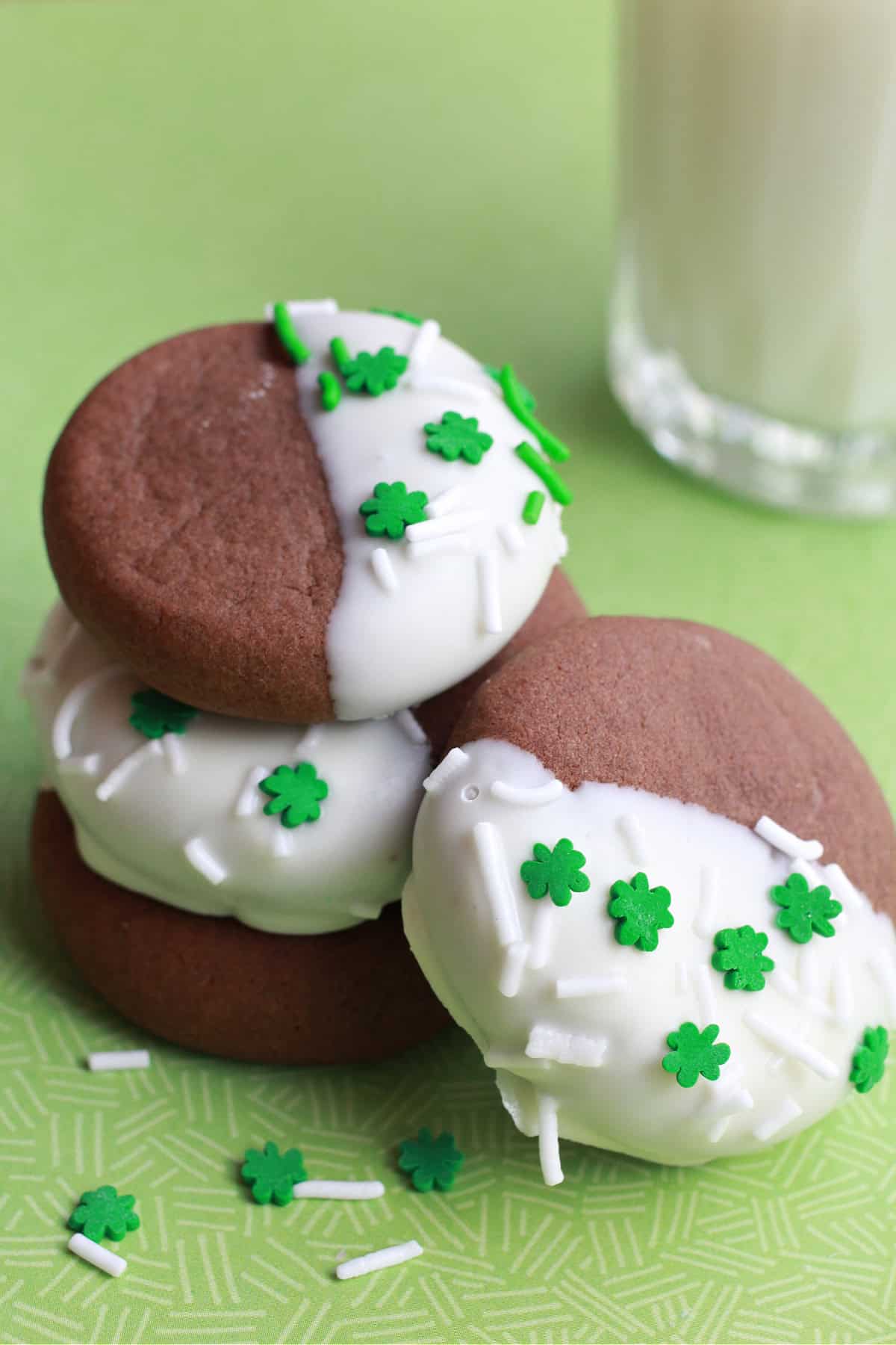 chocolate cookies half dipped in white chocolate with clover leaf sprinkles piled on top of each other.