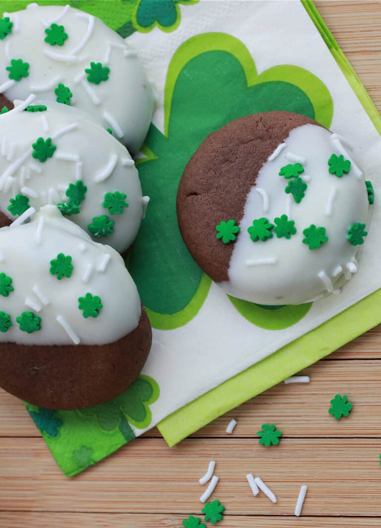 chocolate cookies half dipped in white chocolate with clover leaf sprinkles on a napkin.