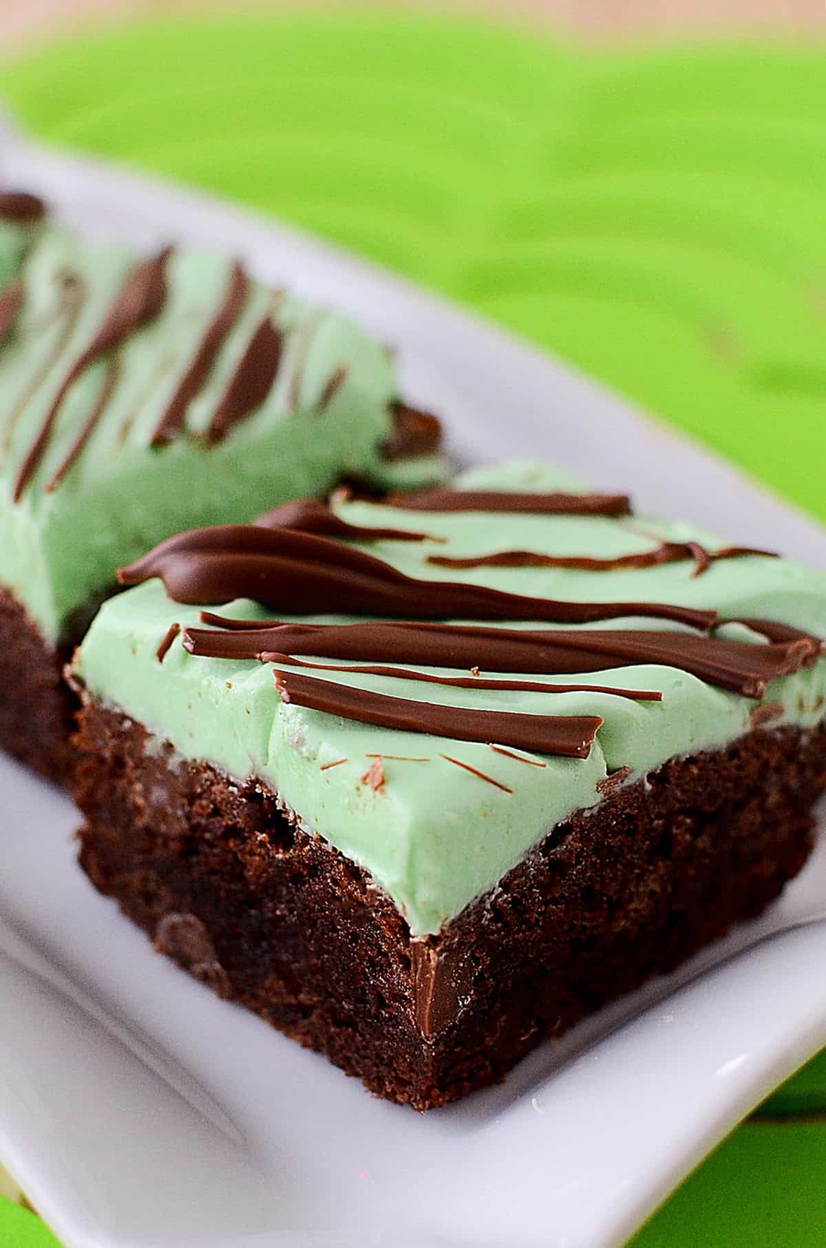 a chocolate brownie with a green frosting on top drizzled with melted chocolate.