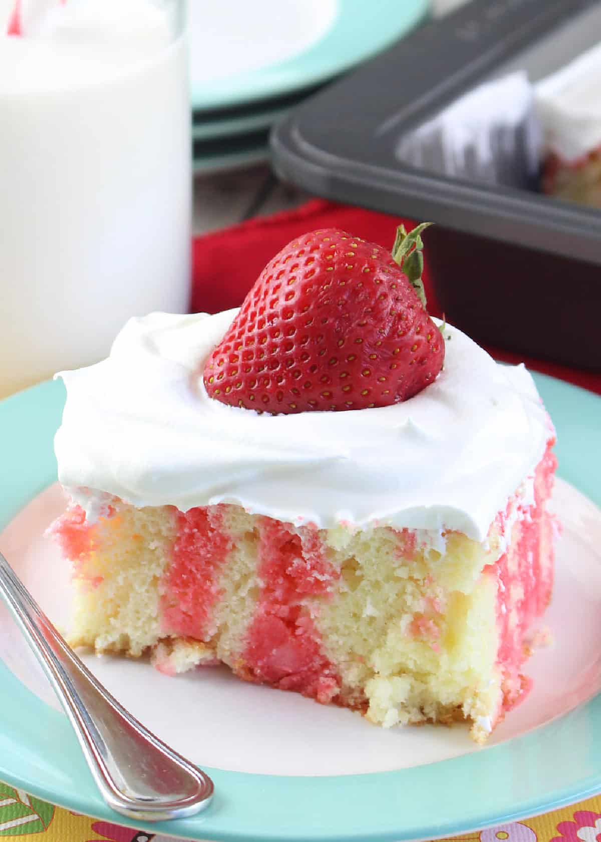 a slice of strawberry poke cake on a plate with a fresh strawberry on top.